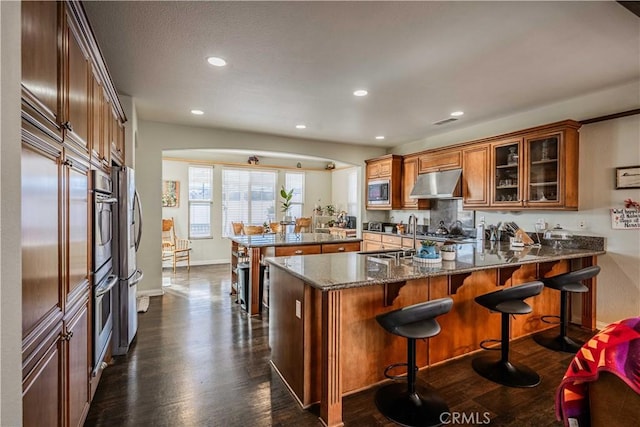 kitchen featuring kitchen peninsula, dark wood-type flooring, sink, dark stone countertops, and stainless steel microwave