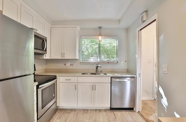 kitchen with white cabinets, hanging light fixtures, sink, light wood-type flooring, and appliances with stainless steel finishes