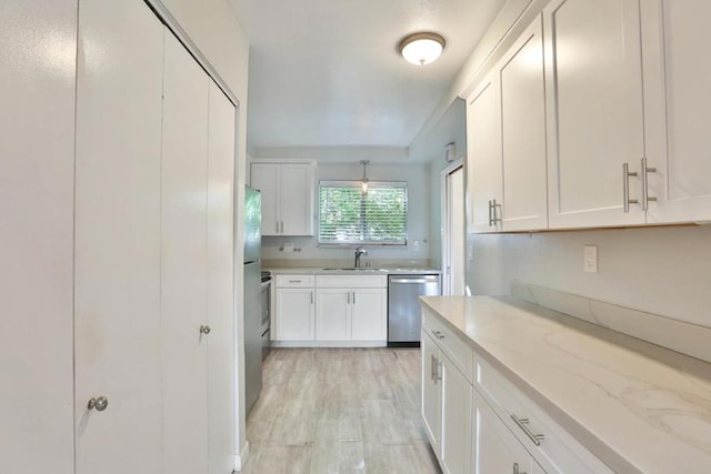 kitchen with white cabinets, sink, light stone countertops, appliances with stainless steel finishes, and light hardwood / wood-style floors