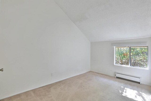 empty room featuring light carpet, a textured ceiling, a baseboard radiator, and vaulted ceiling