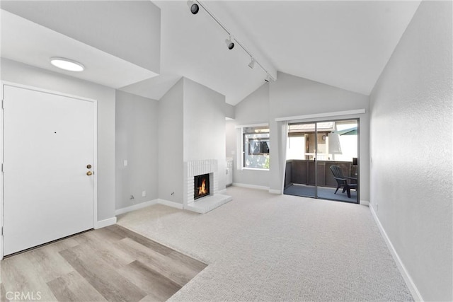 carpeted living room with a fireplace, rail lighting, and high vaulted ceiling