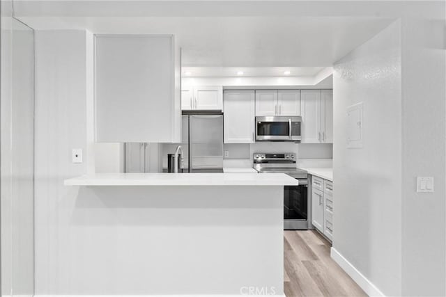 kitchen with kitchen peninsula, white cabinets, stainless steel appliances, and light hardwood / wood-style floors