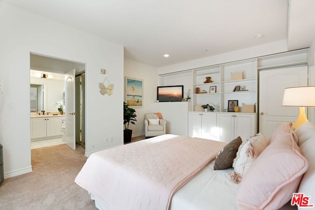 bedroom with a closet, connected bathroom, light carpet, and sink