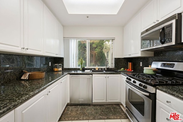 kitchen with white cabinets, backsplash, stainless steel appliances, and dark stone counters