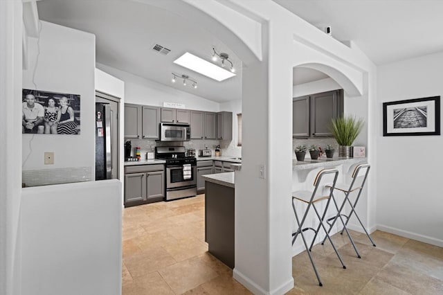 kitchen featuring gray cabinets, appliances with stainless steel finishes, vaulted ceiling with skylight, tasteful backsplash, and light tile patterned floors