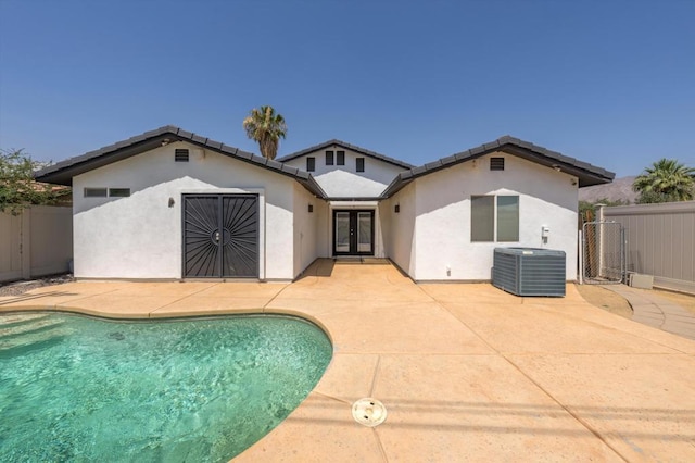 rear view of house with cooling unit, a fenced in pool, a patio area, and french doors