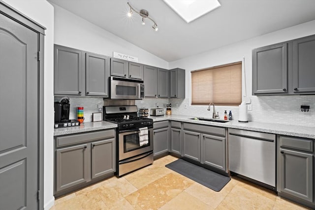 kitchen featuring sink, gray cabinetry, vaulted ceiling, stainless steel appliances, and backsplash