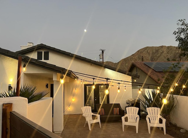 back house at dusk featuring a mountain view and a patio area