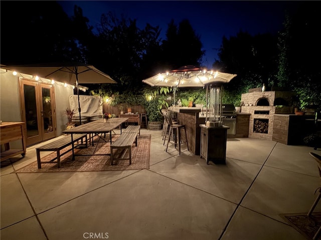 patio at twilight with an outdoor stone fireplace, a bar, grilling area, and exterior kitchen