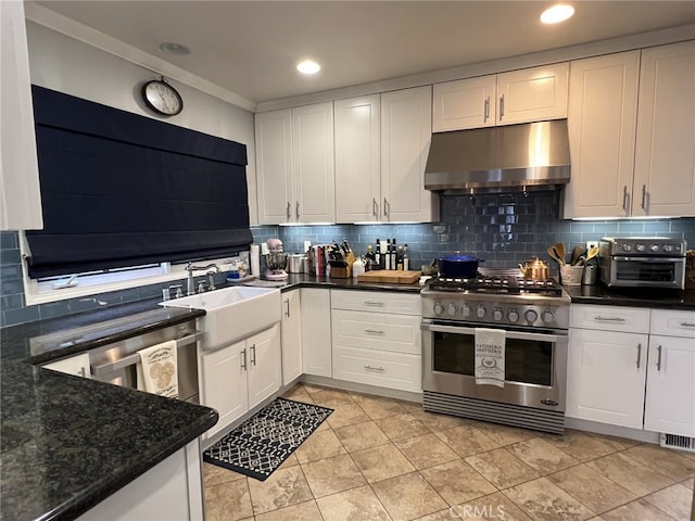 kitchen featuring backsplash, sink, range with two ovens, dark stone countertops, and white cabinetry