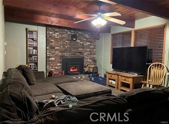 living room featuring beam ceiling, ceiling fan, a fireplace, and wooden ceiling