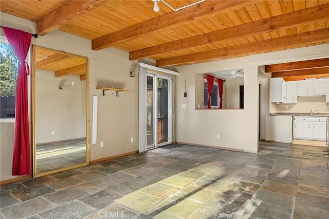 unfurnished living room with baseboards, stone tile floors, wooden ceiling, and beam ceiling