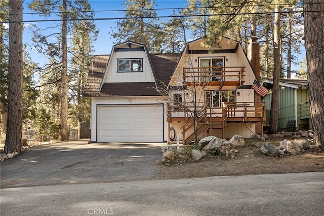 view of front of home featuring a garage, aphalt driveway, stairway, a balcony, and a gambrel roof
