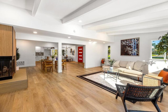 living room with light wood-type flooring, an inviting chandelier, and beamed ceiling