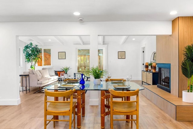 dining space with light hardwood / wood-style flooring, beam ceiling, and a tiled fireplace