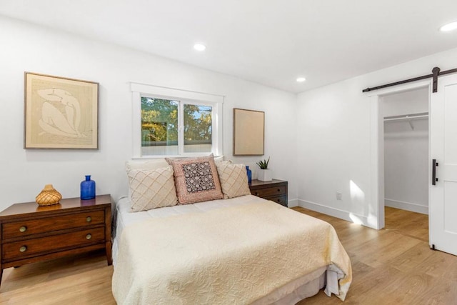 bedroom featuring light wood-type flooring, a barn door, a closet, and a spacious closet