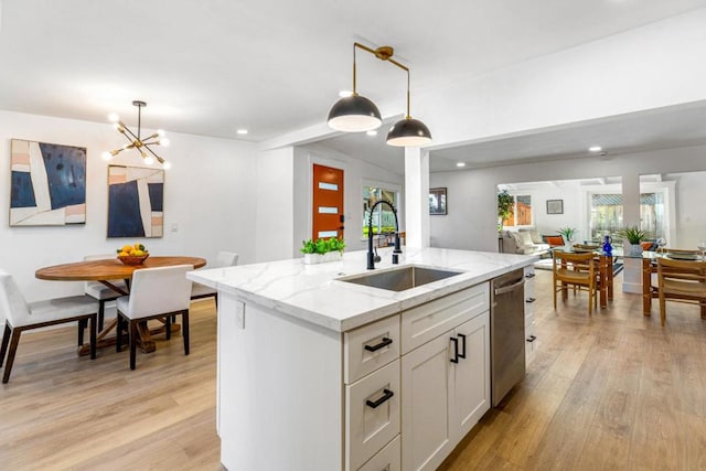 kitchen with sink, white cabinetry, hanging light fixtures, an island with sink, and light stone counters