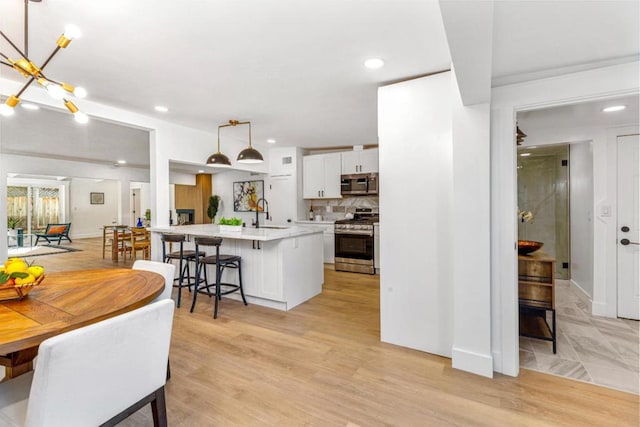 kitchen featuring appliances with stainless steel finishes, a kitchen island with sink, pendant lighting, white cabinets, and a breakfast bar