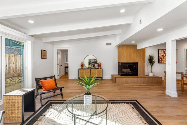 living room featuring a large fireplace, light hardwood / wood-style flooring, and lofted ceiling with beams