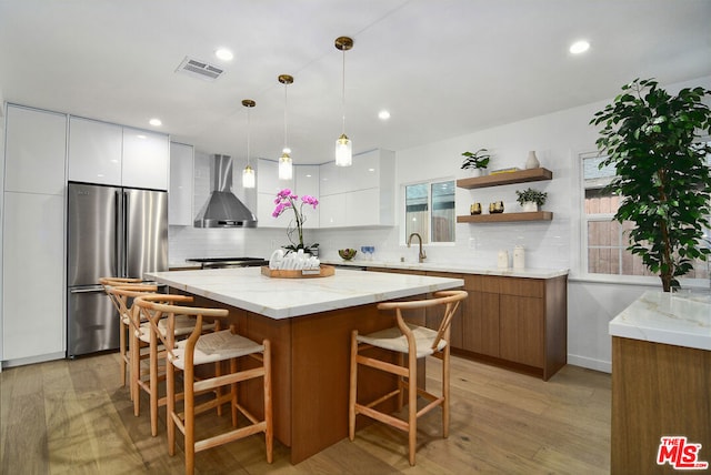 kitchen with high quality fridge, wall chimney range hood, light hardwood / wood-style flooring, a center island, and white cabinetry