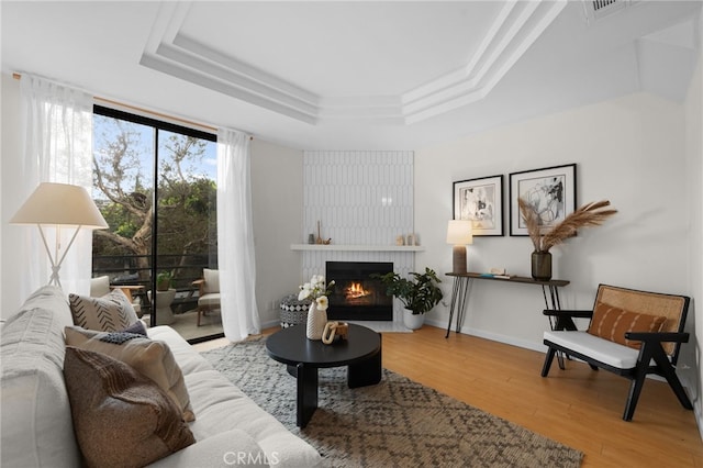 living room with a raised ceiling, a large fireplace, and light hardwood / wood-style floors