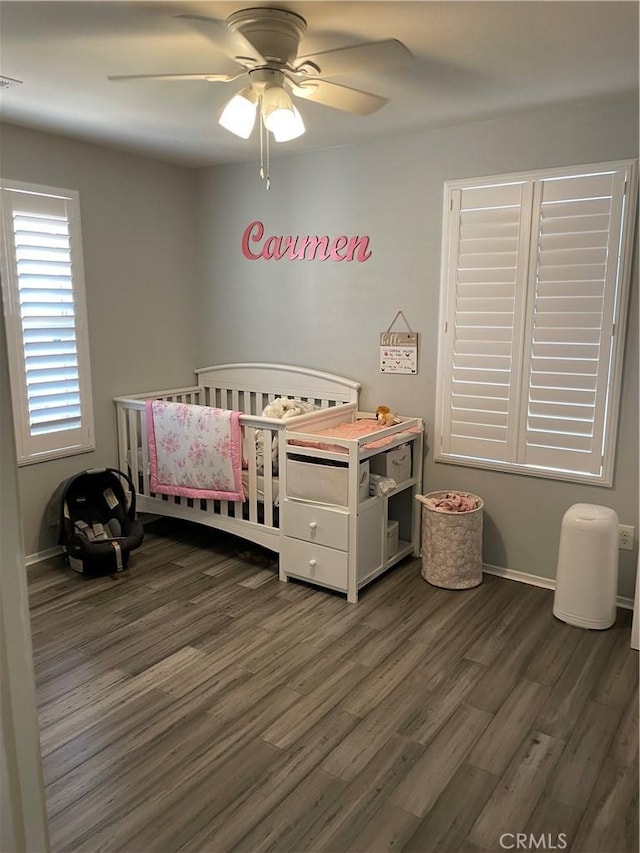 bedroom with dark hardwood / wood-style floors, a nursery area, and ceiling fan