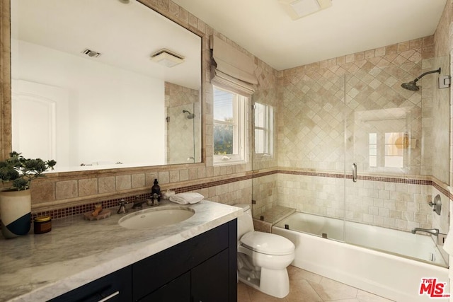 full bathroom featuring vanity, shower / bath combination with glass door, tile patterned flooring, toilet, and tile walls