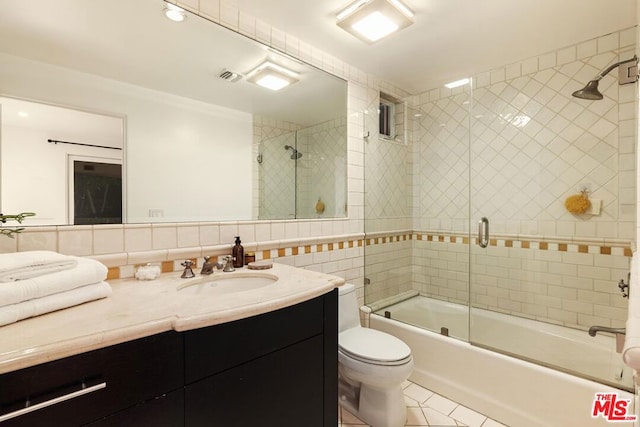 full bathroom featuring vanity, shower / bath combination with glass door, tile patterned flooring, toilet, and tile walls