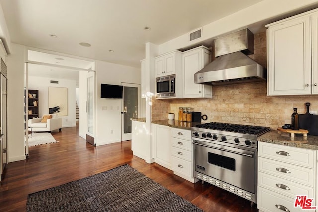 kitchen featuring dark wood-type flooring, white cabinets, wall chimney range hood, decorative backsplash, and appliances with stainless steel finishes