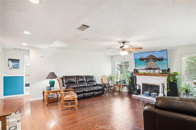 living room featuring a textured ceiling, ceiling fan, dark hardwood / wood-style flooring, and a fireplace