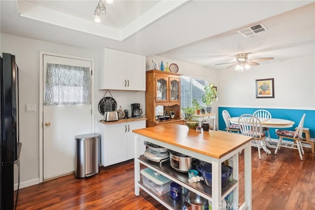 kitchen with a tray ceiling, white cabinetry, black refrigerator, and dark hardwood / wood-style floors