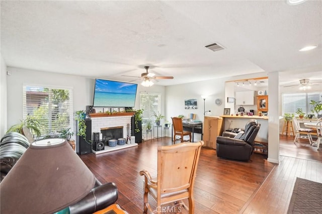 living room featuring ceiling fan, dark hardwood / wood-style flooring, and a brick fireplace