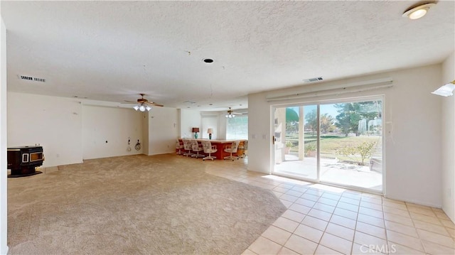 unfurnished living room with ceiling fan, a wood stove, a textured ceiling, and light tile patterned floors