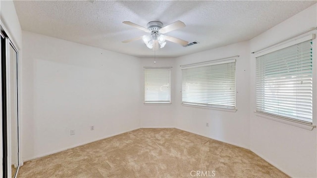 empty room featuring light carpet, ceiling fan, and a textured ceiling