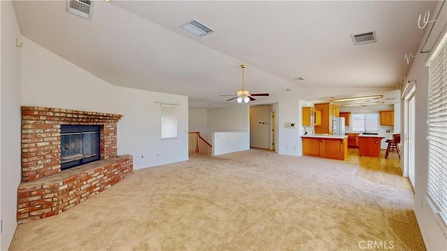 unfurnished living room with light carpet, ceiling fan, lofted ceiling, and a brick fireplace