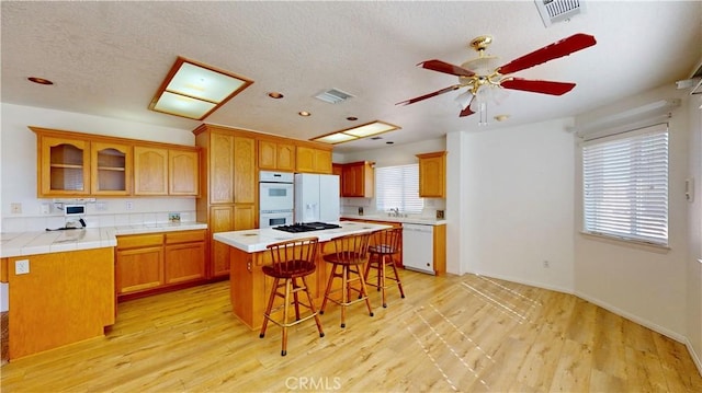 kitchen with a breakfast bar, a center island, white appliances, tile counters, and light hardwood / wood-style floors