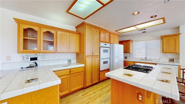 kitchen featuring a center island, white appliances, light hardwood / wood-style flooring, a textured ceiling, and tile counters