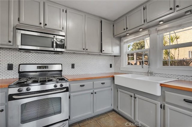 kitchen with sink, decorative backsplash, butcher block countertops, light tile patterned flooring, and stainless steel appliances