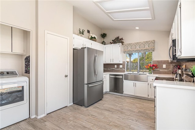 kitchen featuring sink, vaulted ceiling, washer / dryer, white cabinetry, and stainless steel appliances