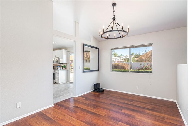 empty room featuring a chandelier, dark hardwood / wood-style floors, and lofted ceiling