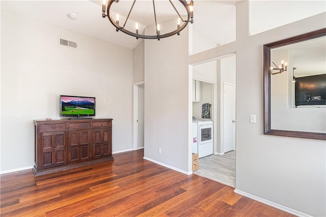 living room featuring washer / clothes dryer, dark hardwood / wood-style flooring, a towering ceiling, and a chandelier