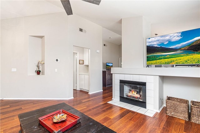 living room featuring a tile fireplace, hardwood / wood-style floors, and high vaulted ceiling