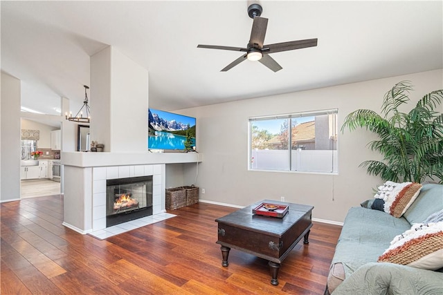 living room with vaulted ceiling, a tiled fireplace, hardwood / wood-style floors, and ceiling fan with notable chandelier