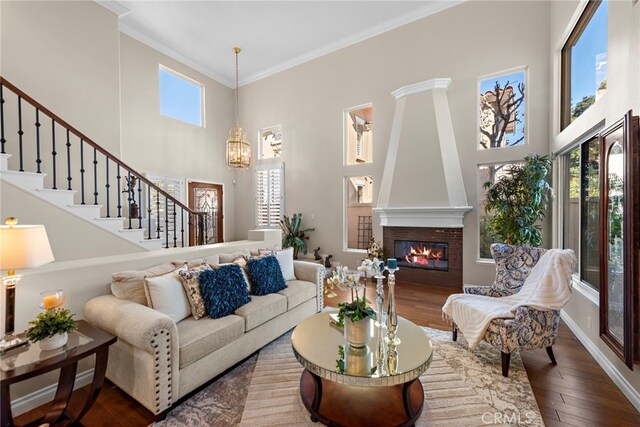 living room with dark hardwood / wood-style flooring, ornamental molding, a large fireplace, an inviting chandelier, and a high ceiling