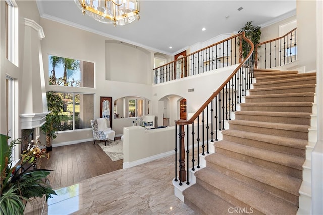 entryway with wood-type flooring, crown molding, a high ceiling, and a chandelier