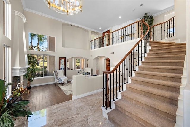 stairs with baseboards, ornamental molding, arched walkways, and a notable chandelier