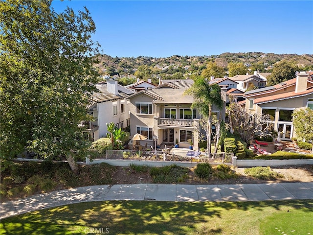 back of house featuring a balcony, a fenced front yard, and stucco siding