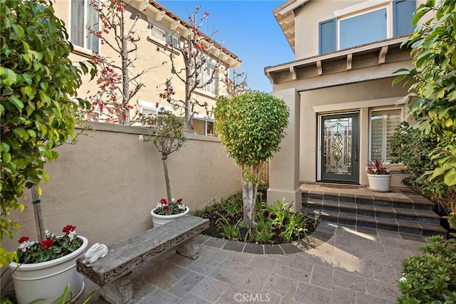 view of exterior entry with fence and stucco siding