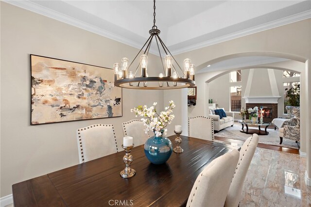 dining area featuring light hardwood / wood-style flooring, a large fireplace, crown molding, and an inviting chandelier