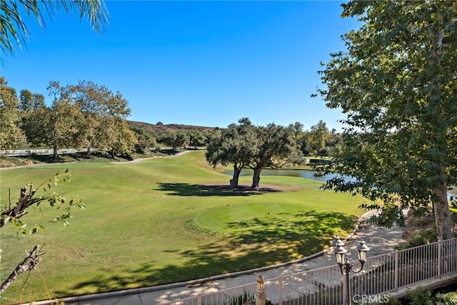 surrounding community featuring a water view, view of golf course, fence, and a yard